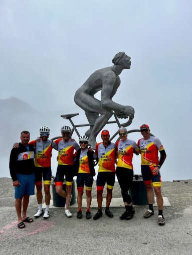 Group of HC Bike Tours guests and staff posing for a picture at the "The Giant of Tourmalet" (Le Géant du Tourmalet) scultpure in honor of Octave Lapize, the first rider to cross the Col du Tourmalet in the Tour de France in 1910. French Pyrenees bike trip, July 2023.