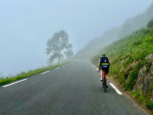 Cyclists riding up to Col d'Aspin in the morning mist during bike trip in French Pyrenees in July 2023