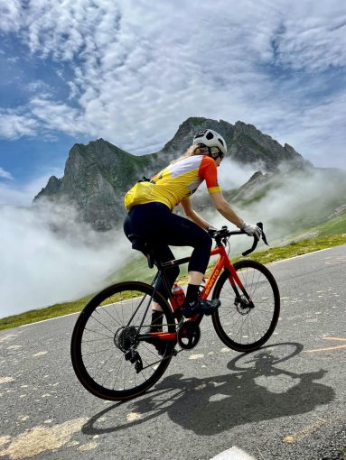 Cyclists riding up to Col du Tourmalet with mountain peaks and clouds in the background, during French Pyrenees bike trip in July 2023