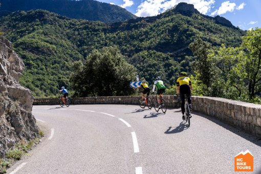 Cyclists navigating a curve surrounded by mountains.