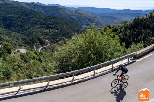 Cyclist navigating a curve before the downhill, surrounded by mountains.