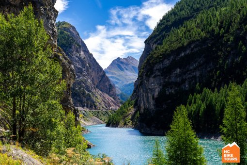 Turquoise river winding through a valley, surrounded by pine trees and towering mountain peaks.